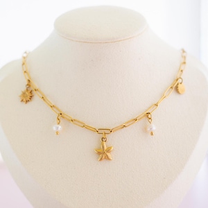 Può includere: Collana a catena dorata con più ciondoli, tra cui una stella marina, un sole e due perle.