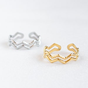 Könnte beinhalten: Zwei verstellbare Ringe mit Zickzack-Muster. Ein Ring ist silber und der andere ist gold.