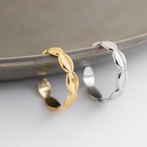 Könnte beinhalten: Zwei verstellbare Ringe mit einem Blattdesign. Der Ring links ist golden und der Ring rechts ist silber.