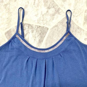 May include: A blue camisole top with thin spaghetti straps. The neckline is trimmed with a silver sequined band. The top has a gathered detail below the neckline. The fabric appears to be a soft knit material.