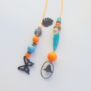 May include: Two orange and blue beaded necklaces with charms. One necklace has a butterfly charm and the other has a bell charm.