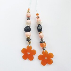 May include: Two orange flower charms with a white string and beads in shades of pink, black, and gold.
