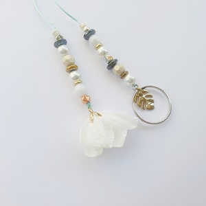 May include: Two white beaded necklaces with gold and silver accents. One necklace has a white flower charm and the other has a gold leaf charm on a silver ring.