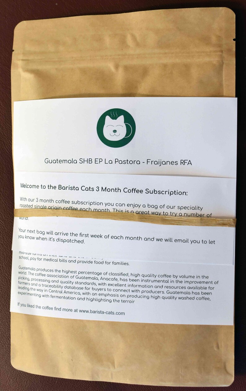 A brown paper coffee bag with a white label featuring a green circular logo of a cat face. The label includes the text Guatemala SHB EP La Pastora - Fraijanes RFA and information about a Barista Cats 3 Month Coffee Subscription.
