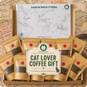 May include: A cardboard gift box containing twelve small brown pouches of coffee beans, each labelled with a red numbered sticker. A large white card inside features a world map with numbered locations and the text Around the World in 12 Coffees.