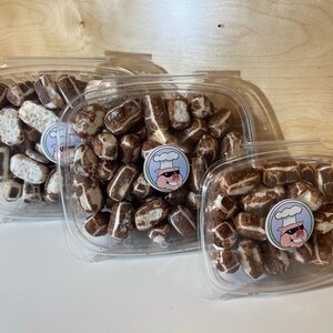 May include: Three clear plastic containers filled with chocolate-covered pretzels. The containers are of different sizes and are stacked on top of each other. The pretzels are arranged in a random pattern and are all covered in a thin layer of chocolate.