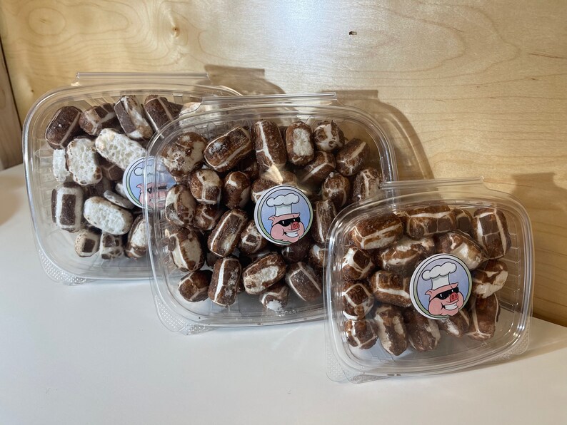 May include: Three clear plastic containers filled with chocolate-covered pretzels. The containers are of different sizes and are stacked on top of each other. The pretzels are arranged in a random pattern and are all covered in a thin layer of chocolate.