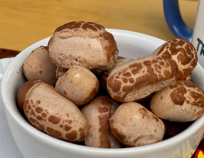 May include: A white bowl filled with brown, textured, peanut-shaped snacks.