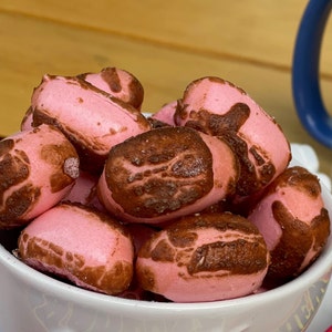 May include: A white bowl filled with pink and brown chocolate-covered marshmallows. The marshmallows are arranged in a pile and have a slightly irregular shape.