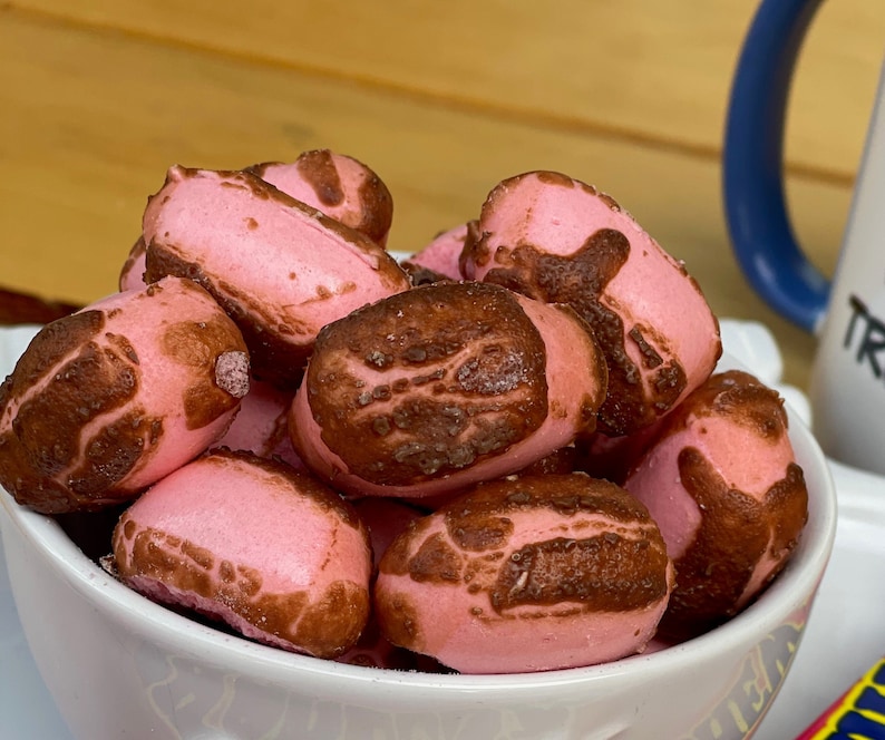 May include: A white bowl filled with pink and brown chocolate-covered marshmallows. The marshmallows are arranged in a pile and have a slightly irregular shape.