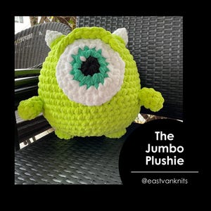 May include: A green and white crocheted plush toy shaped like a monster with one large eye. The toy is sitting on a black wicker chair. The text "The Jumbo Plushie @eastvanknits" is below the toy.