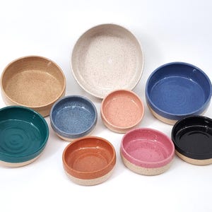 May include: Set of ten ceramic bowls in various colors and sizes. The bowls are speckled with white and have a smooth, rounded rim.