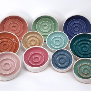 May include: A set of ten ceramic slow feeder bowls in various colors, including pink, blue, green, and brown. Each bowl has a raised, circular design in the center.