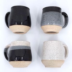 May include: Four ceramic mugs with speckled designs and neutral-colored bases. The mugs feature black, gray, and white speckled patterns. Each mug has a rounded shape with a handle. The mugs are ideal for coffee or tea.