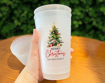 May include: A frosted plastic cup with a Christmas tree design and the words "MERRY Christmas" and "THE SMITH FAMILY" in red script. The cup is held in a hand, with a second cup visible in the background.