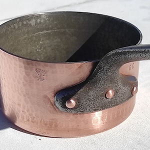 May include: A copper saucepan with a hammered finish and a dark metal handle attached with rivets. The interior is a darker metal. The word "FAVOR" is stamped on the side.