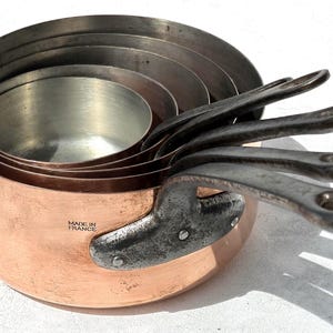 Peut inclure: Un ensemble de quatre casseroles en cuivre emboîtables avec des poignées en métal sombre, dotées d'un intérieur métallique et de l'inscription MADE IN FRANCE estampillée sur le côté de la plus grande. Les casseroles sont empilées.