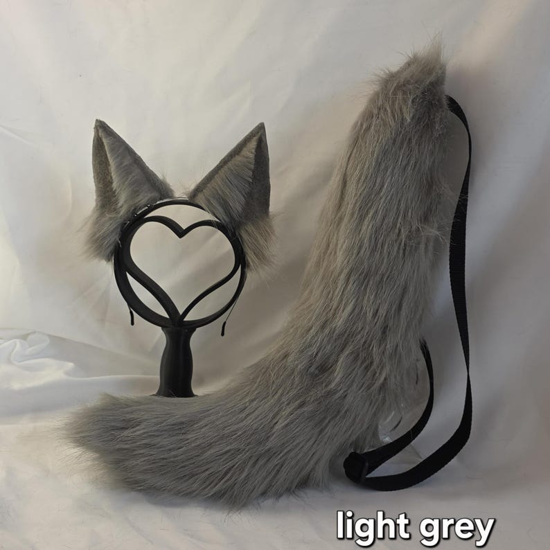May include: A light grey faux fur cosplay set featuring a headband with ears and a tail. The ears are triangular and attached to a black headband. The tail has a black strap. The text "light grey" is visible.