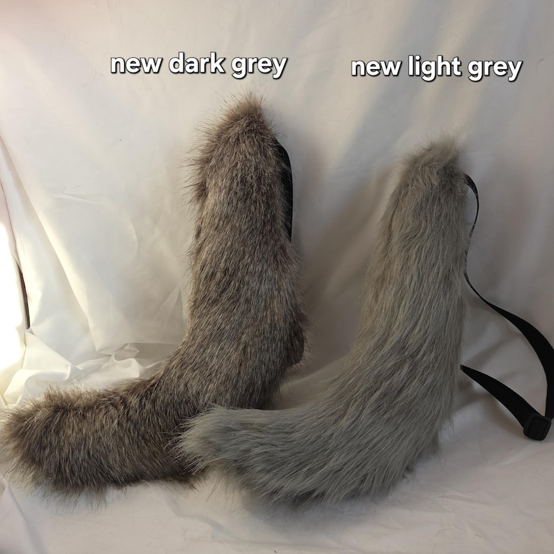 May include: Two faux fur tails, one dark grey and one light grey, with black straps. The tails are fluffy and have a curved shape. Text at the top reads "new dark grey" and "new light grey".