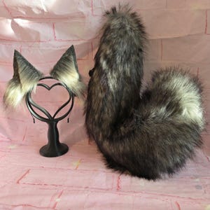 Puede incluir: Un conjunto de disfraz de lobo de piel sintética con una diadema con orejas y una cola a juego. Las orejas son grises y blancas, y la cola es una mezcla de gris, marrón y blanco. Para cosplay o fiestas de disfraces.