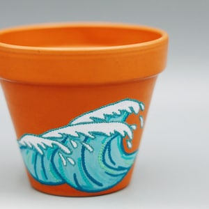 May include: Orange terracotta planter with a hand-painted design of blue and white waves.