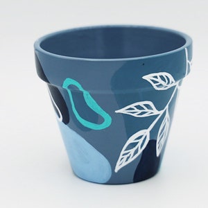 May include: A blue ceramic planter with white and teal abstract designs. The planter is painted with a floral pattern.
