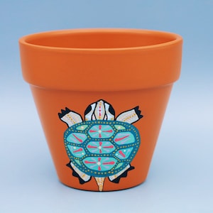 May include: A terracotta flower pot featuring a hand-painted turtle design. The turtle is blue, green, pink, and white with gold accents.