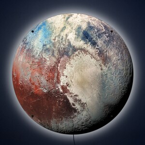 May include: A round wall art piece depicting the surface of Pluto. The artwork features a detailed, colorful rendering of the dwarf planet, with shades of red, white, blue, and brown. The piece has a glowing halo effect and is mounted with small black fasteners.