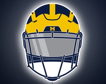 May include: A white and blue football helmet with a yellow face mask and a large "M" on the front. The helmet is illuminated with a white light.