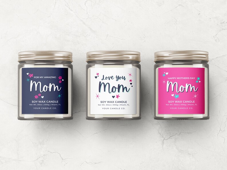 May include: Three glass soy wax candles with gold lids and labels. The labels are white, pink, and blue with the word "Mom" in a decorative font. The labels also include the text "Soy Wax Candle", "Net Wt. 000g | Miami, FL", and "Your Candle Co.".