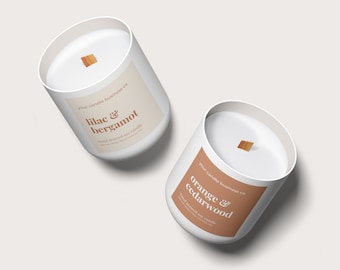 May include: Two white soy candles with wooden wicks. One candle has a label that reads "lilac & bergamot", and the other reads "orange & cedarwood". The labels are tan with white text. The candles are from "your candle business co."