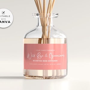 Könnte beinhalten: Eine klare Glasflasche mit einem rosa Etikett, auf dem "Wild Rose & Geranium Scented Reed Diffuser" steht. Die Flasche ist mit einer klaren Flüssigkeit gefüllt und hat Holzstäbchen, die hineingesteckt sind.