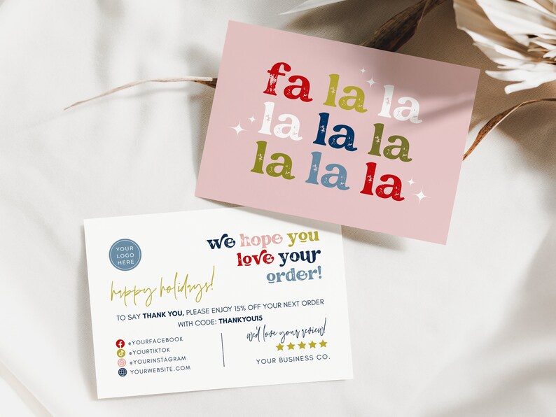 May include: Two holiday-themed cards. One pink card features the phrase "fa la la la" in red, green, blue, and white, with star accents. The second card is white with text in gold, red, and blue, including "happy holidays!" and "We hope you love your order!"