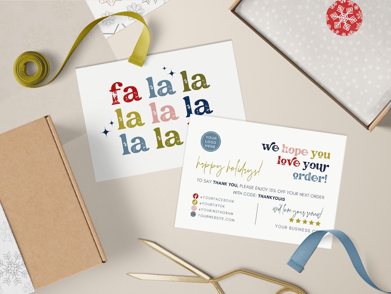 May include: A flat lay featuring holiday-themed stationery. Two cards display the text "fa la la" and "We hope you love your order!" with a festive design. A brown box, ribbon, and scissors are also present.