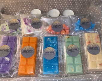 May include: A collection of wax melts in various colors and scents, including lavender, orange, blue, green, and white. The wax melts are packaged in clear plastic bags with a label that says "Sassy Scents".