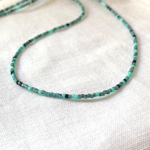 May include: A finely crafted necklace featuring tiny beads in a mix of turquoise, teal, and black. The necklace is presented against a white backdrop, highlighting the detailed beadwork and colour variations. This simple necklace is an elegant accessory.