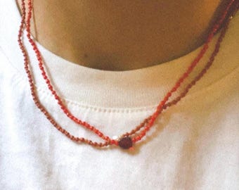 May include: A layered necklace with two strands of small red beads and a single red heart charm.