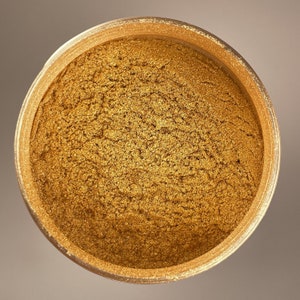 May include: A close-up of a container filled with gold glitter. The glitter is fine and shimmery, and it is ideal for adding a touch of sparkle to any project.