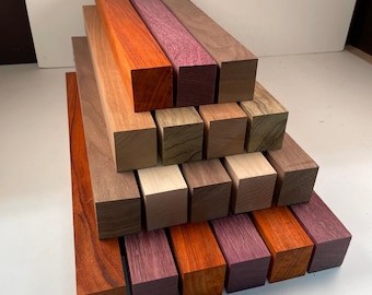 May include: A collection of various hardwood blocks in shades of red, orange, purple, and brown. The blocks are rectangular and stacked, showcasing the natural wood grain and color variations. Ideal for woodworking projects.