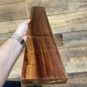 May include: A long, narrow piece of wood with a rich, dark brown colour and a distinctive grain pattern. The wood has a smooth, polished finish.
