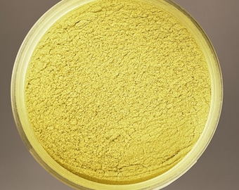 May include: A container filled with a finely milled, light yellow powder. The powder has a textured appearance, suggesting it is a cosmetic product, such as eyeshadow or pigment. The container is clear, allowing the color of the powder to be fully visible.
