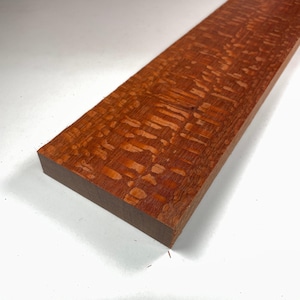 May include: A close-up of a piece of wood with a reddish-brown colour and a unique, swirling grain pattern.