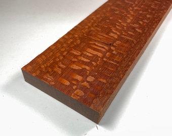 May include: A close-up of a piece of wood with a reddish-brown color and a unique, swirling grain pattern.