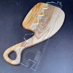May include: A wooden cutting board with a unique shape and a clear plastic template overlay. The template has markings for different cuts, including "round cut center prime" and "round cut center prime". The template also has the date "09:01:14" printed on it.