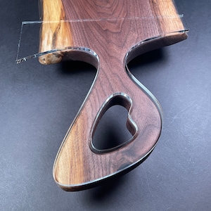 May include: A large, dark brown wooden chopping board with a heart-shaped cutout. The board has a natural wood grain and is finished with a clear epoxy resin.
