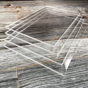 May include: Four clear acrylic sheets stacked on top of each other on a wooden surface.
