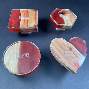 May include: Four different shaped coasters made of wood and resin. The coasters are red and brown with a clear epoxy finish. Each coaster has a clear label with a number on it. The coasters are 02-015, 02-016, 02-017, and 02-018.