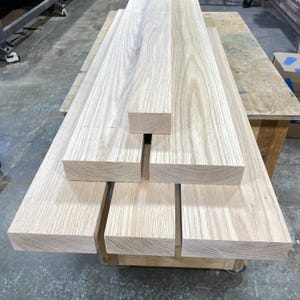 Peut inclure: Une pile de cinq planches en bois rectangulaires de couleur claire avec des motifs de grain visibles. Les planches sont disposées en formation étagée, mettant en valeur les surfaces lisses et poncées ainsi que les tons naturels de bois brut.