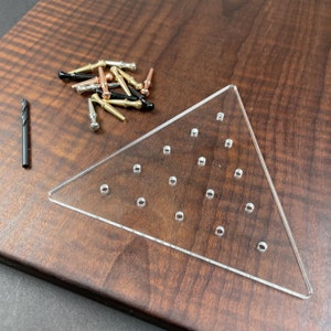 May include: A clear acrylic triangle-shaped board with 25 holes for holding small items. The board is on a wooden surface with a variety of small metal and plastic items scattered around it.