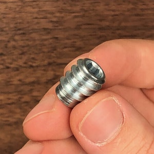 May include: A silver metal screw insert with a threaded design. The insert is designed to be used in wood or other materials to create a strong and durable connection.